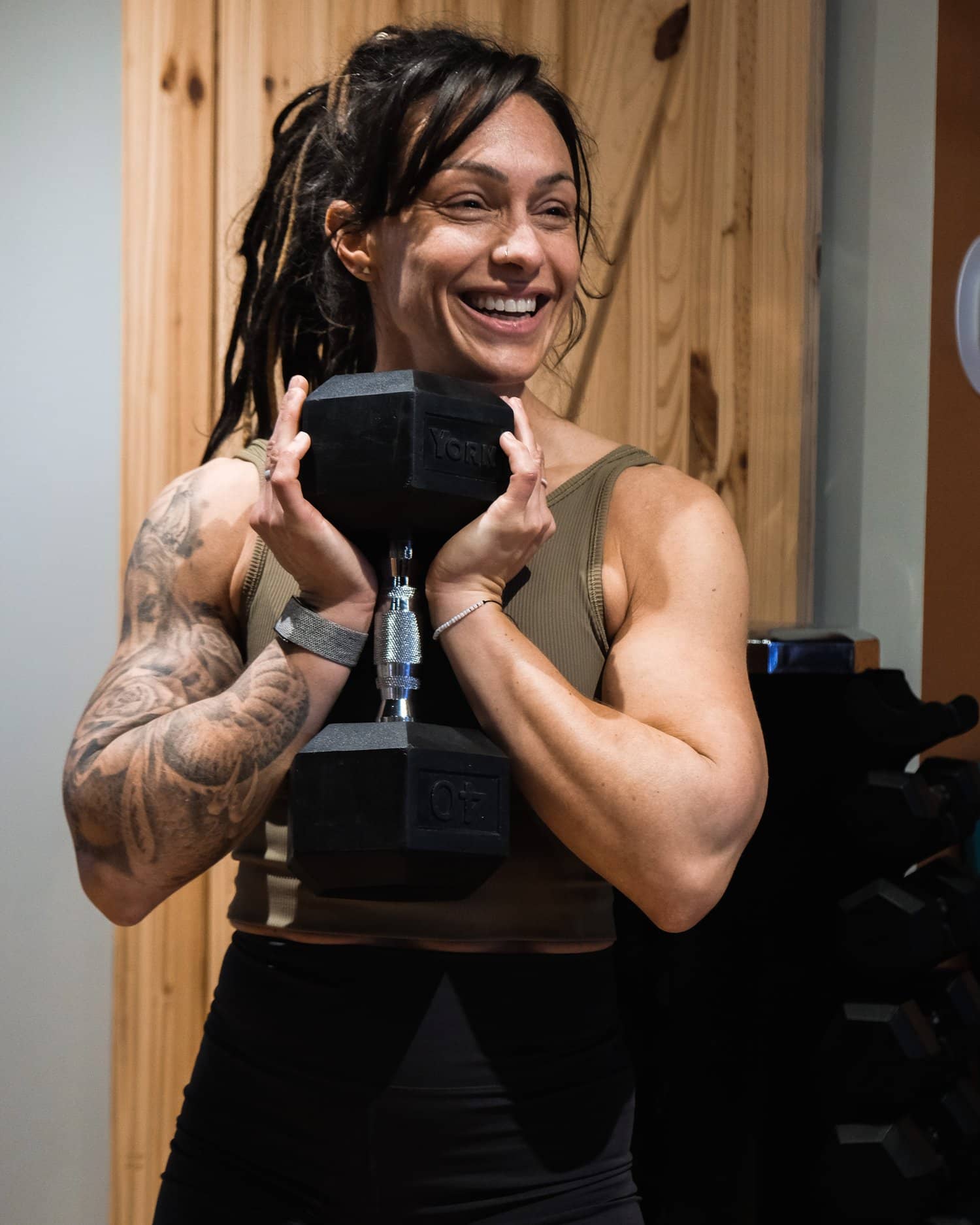 Jess Zawadowicz, founder of Bar None Fitness Studio, smiling with a dumbbell held at her chest in the Burlington studio